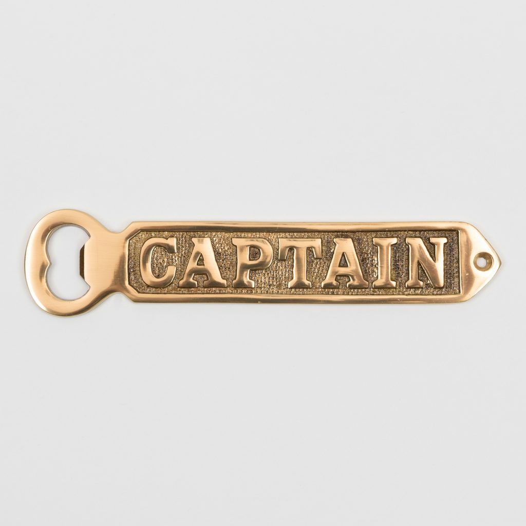 A solid brass bottle opener with 'Captain' written on it. Photographed on a white background.