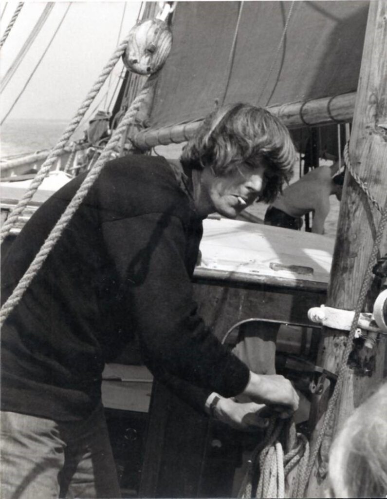 A black and white photo of John Cunliffe sailing with a cigarette in his mouth.