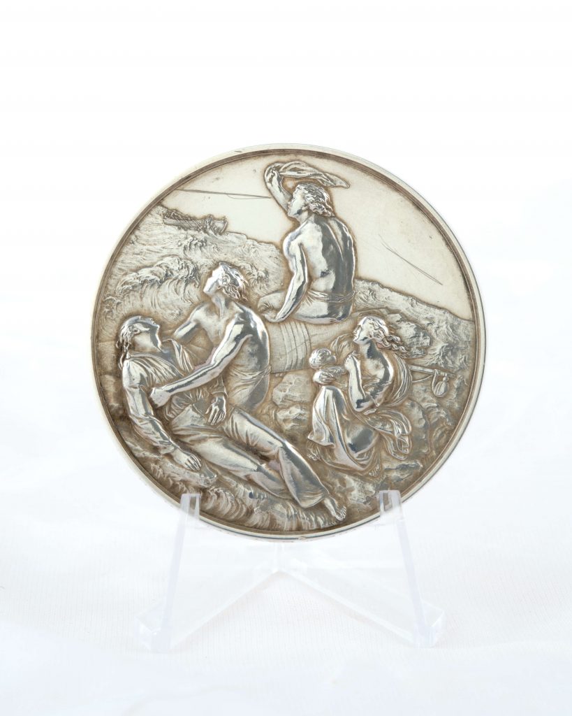 A silver medal awarded to William Barker for his bravery in saving lives at sea during the Great Blizzard of 1891. Barker was one of the three men who crossed on the breeches buoy to rescue the crew of the Bay of Panama, which was shipwrecked off the coast of the treacherous Lizard Peninsula. It has a very intricate scene of a shipwreck, reminiscent of The Raft of the Medusa by Géricault. It's on loan to NMMC from the Barker family.