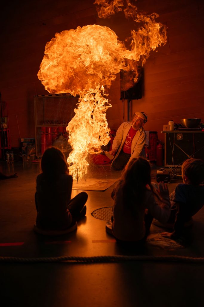 An explosion during a science show. A ball of flame is rising with children looking onwards.