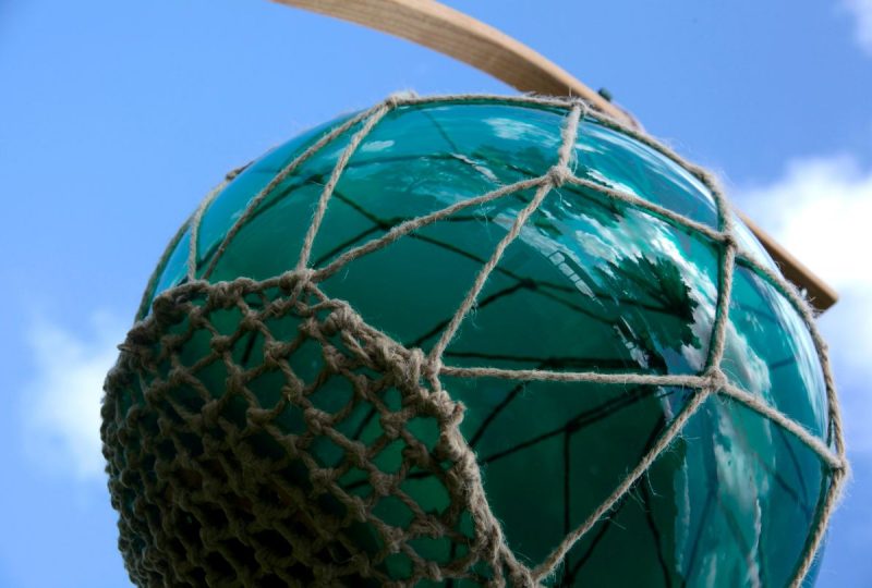 A hanging green glass buoy pictured against a blue sky.