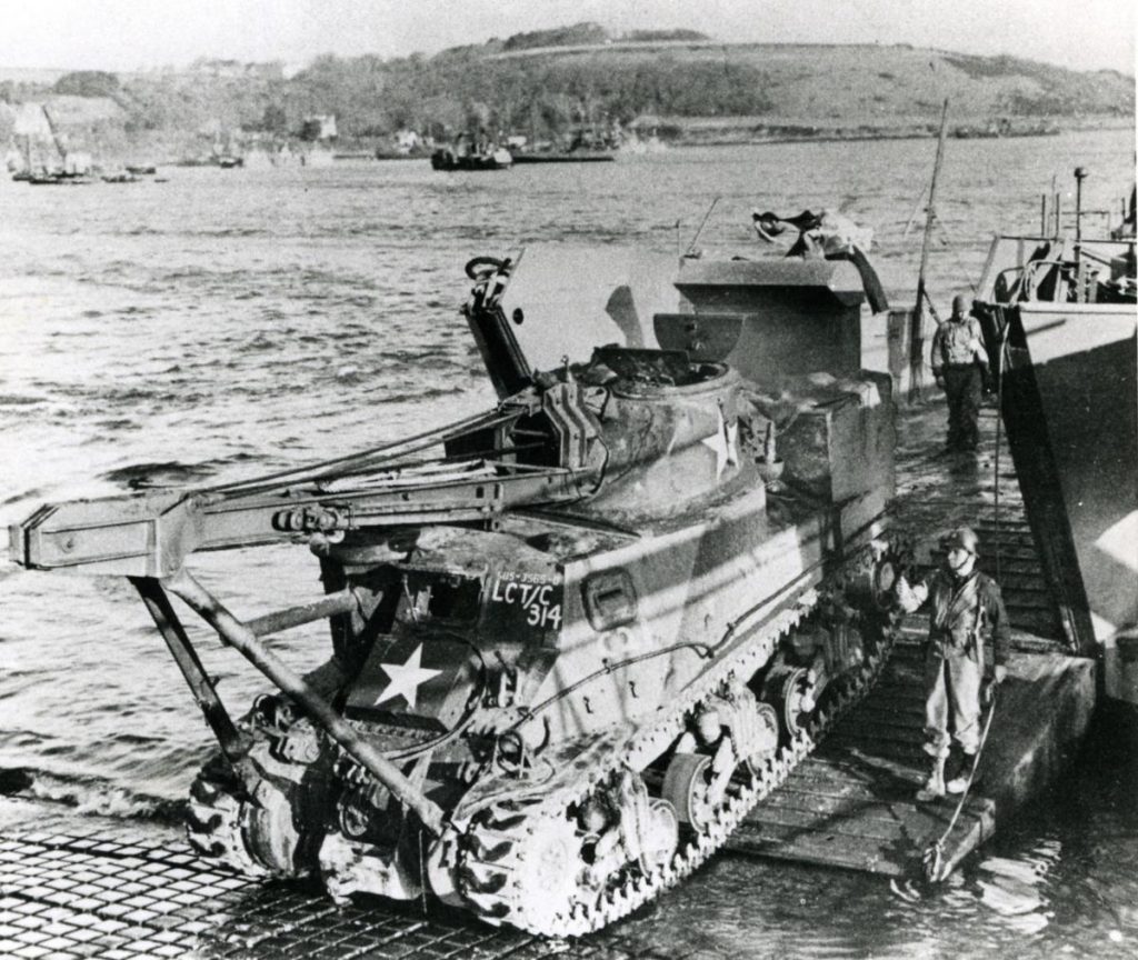 A tank landing craft embarks an Armoured Recovery Vehicle, an obsolete General Lee tank fitted with a crane and powerful winches to recover disabled tanks on the battlefield