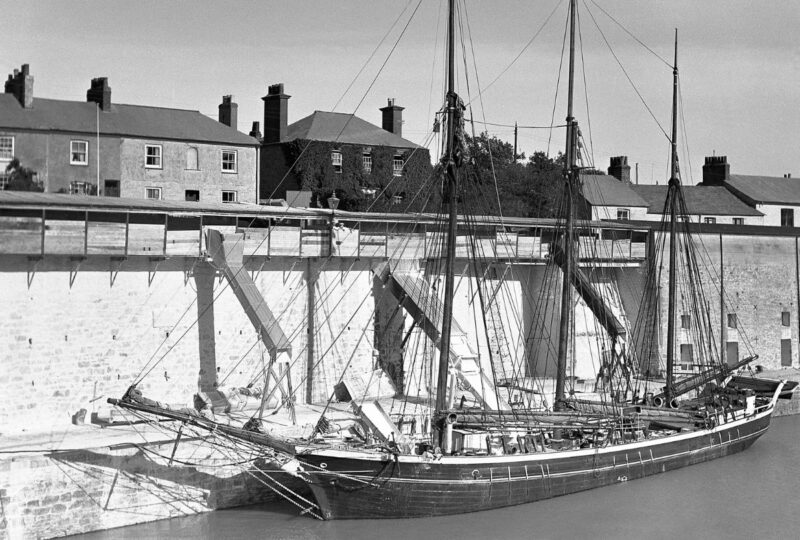 A black and white photo of the schooner Fortuna loading clay from dockside chutes in Charlestown Harbour, 1934.