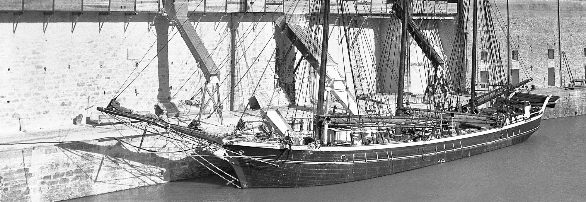 A black and white photo of the schooner Fortuna loading clay from dockside chutes in Charlestown Harbour, 1934.