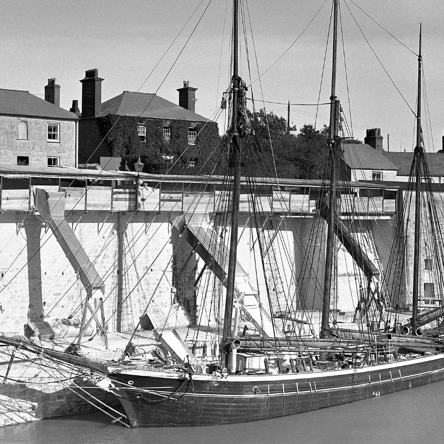 A black and white photo of the schooner Fortuna loading clay from dockside chutes in Charlestown Harbour, 1934.