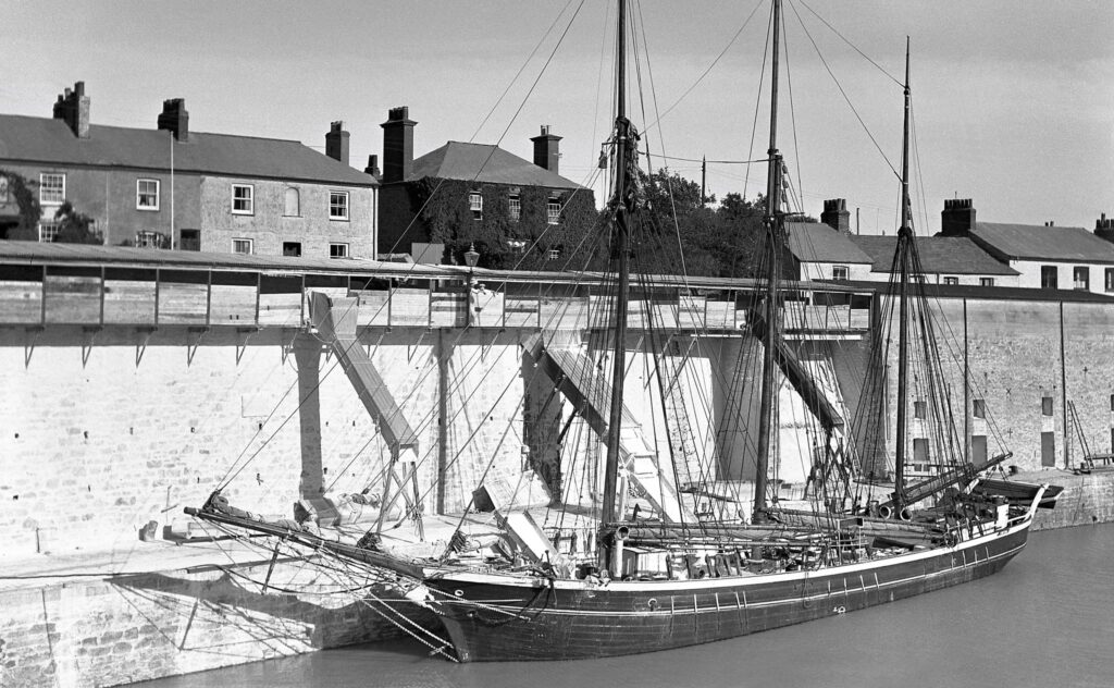 A black and white photo of the schooner Fortuna loading clay from dockside chutes in Charlestown Harbour, 1934.