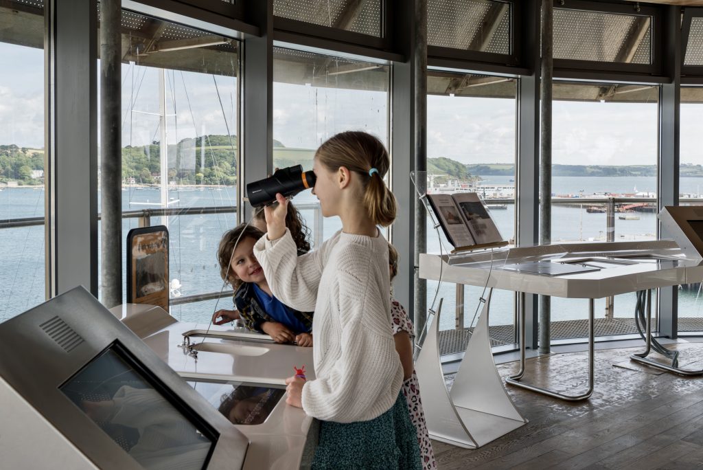 Children in the Lookout Tower at National Maritime Museum Cornwall. A girl looks through binoculars across the harbour.