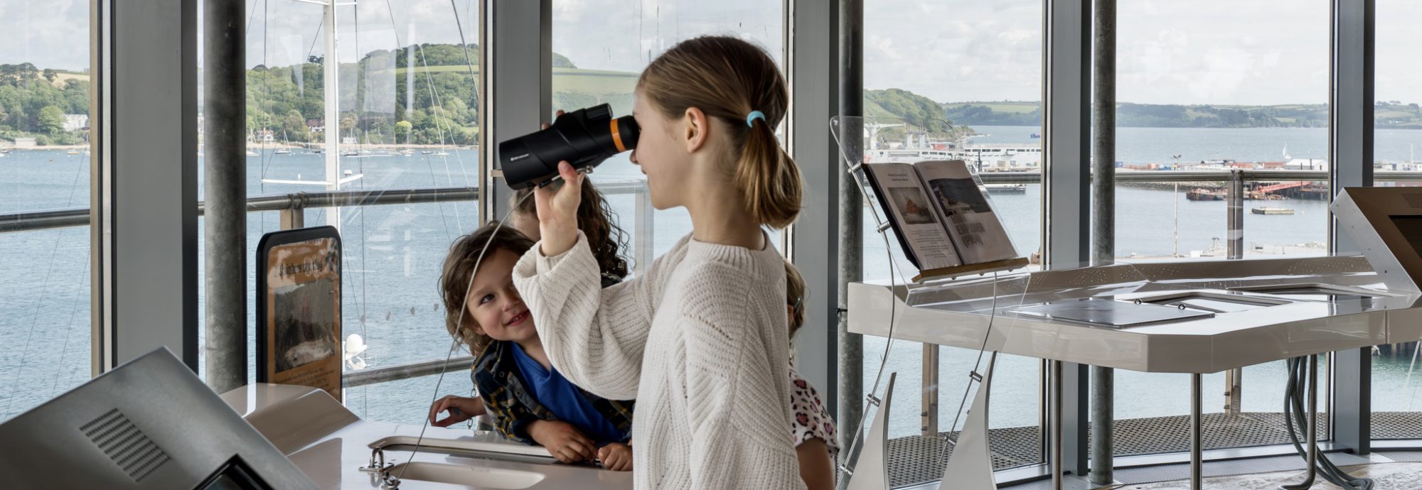 Children in the Lookout Tower at National Maritime Museum Cornwall. A girl looks through binoculars across the harbour.