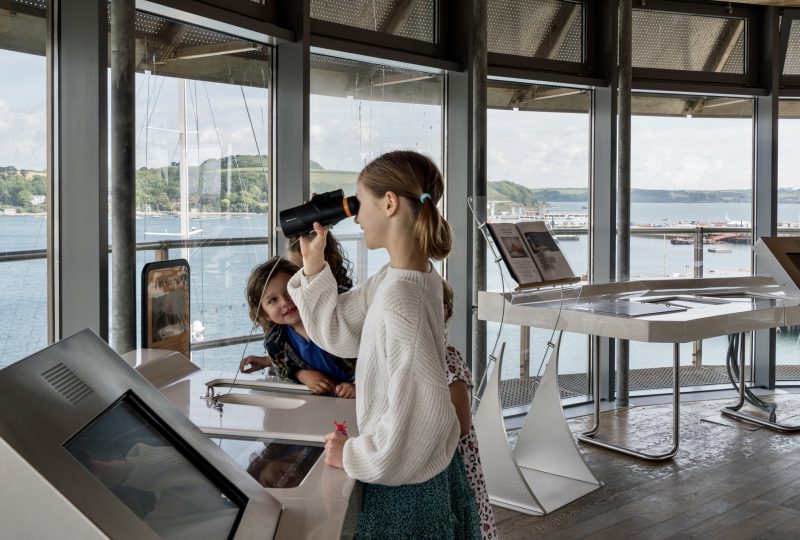 Children in the Lookout Tower at National Maritime Museum Cornwall. A girl looks through binoculars across the harbour.