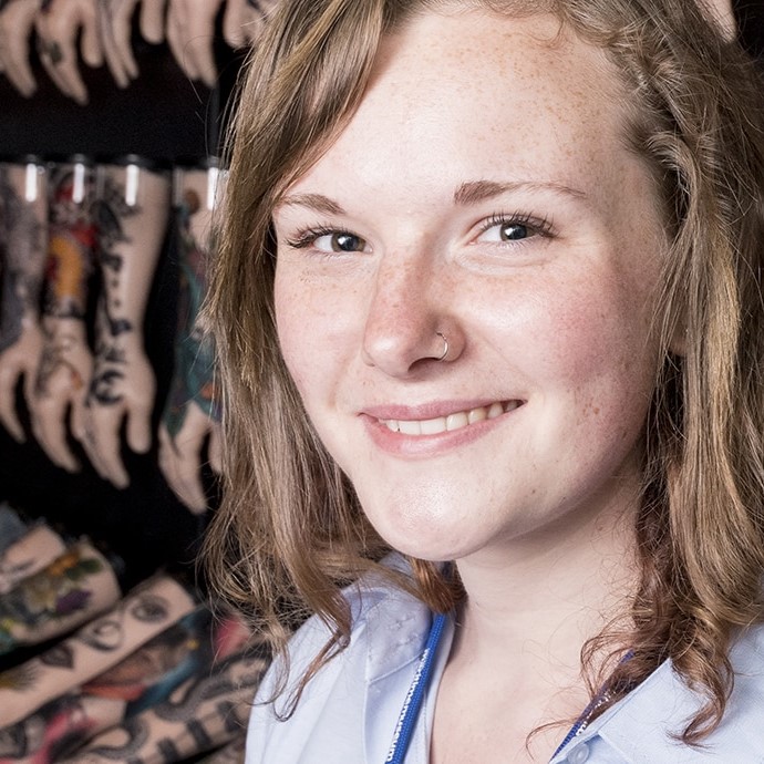 Image of a female volunteer against a wall of tattooed silicone hands.