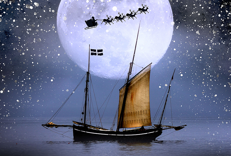 An image of a sailing boat at sea in front of a large moon with Father Christmas being pulled by reindeer in the sky.