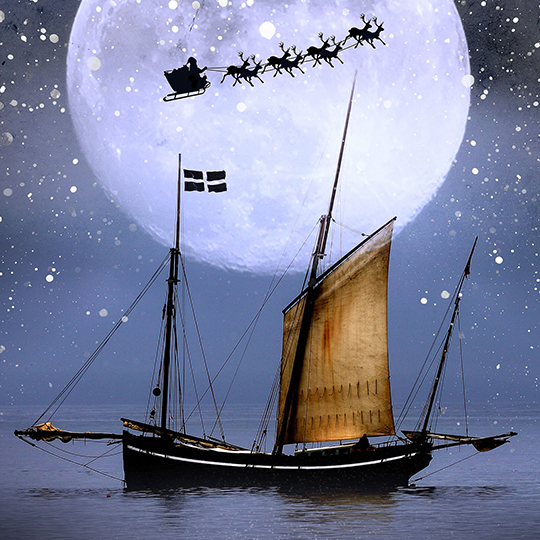 An image of a sailing boat at sea in front of a large moon with Father Christmas being pulled by reindeer in the sky.