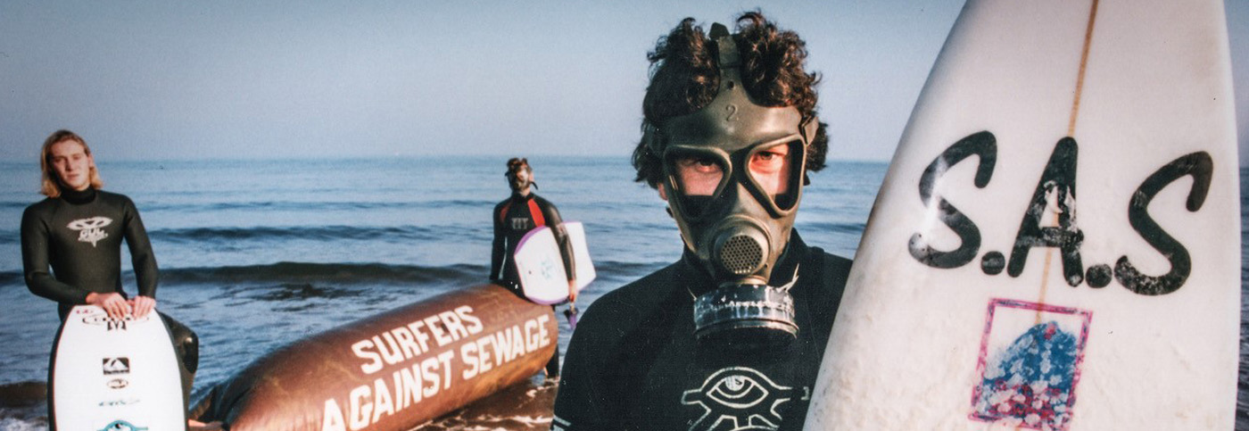 Chris Hines SAS Campaigner holding an SAS branded surfboard and wearing a wetsuit.