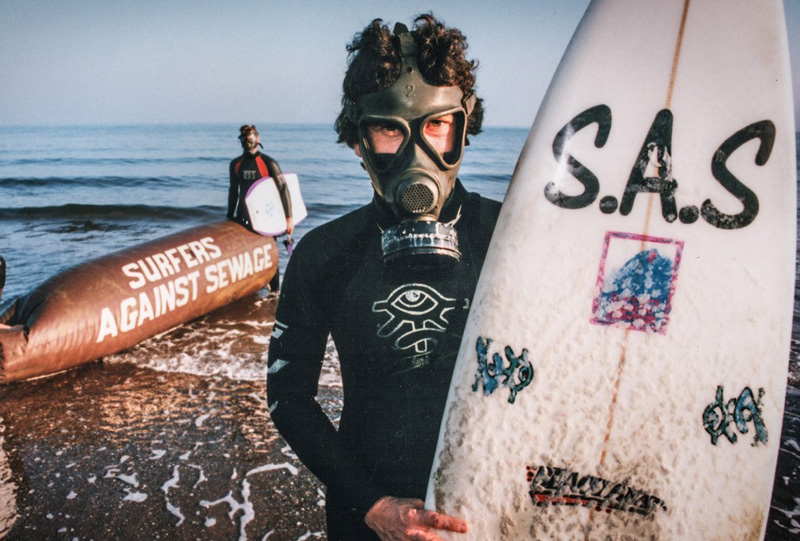 Chris Hines SAS Campaigner holding an SAS branded surfboard and wearing a wetsuit.