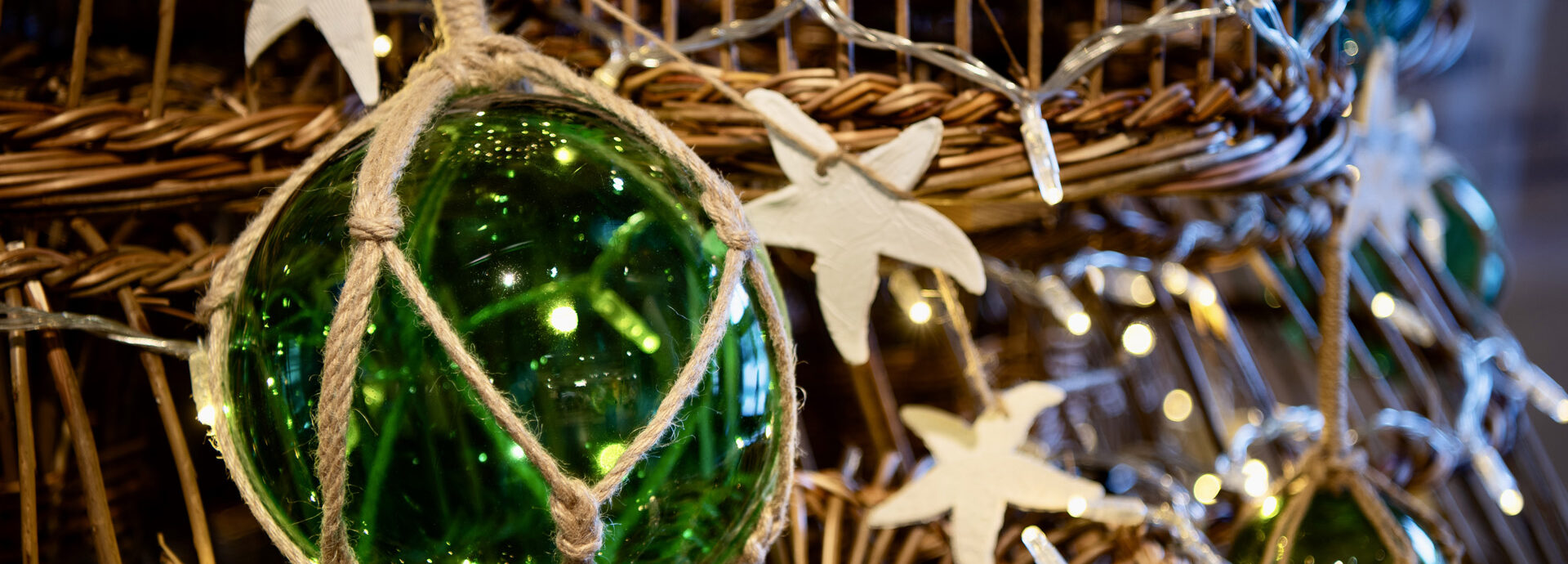 A close-up image of a green glass buoy tired to a lobster pot, with fairy lights and starfish decorations around it.