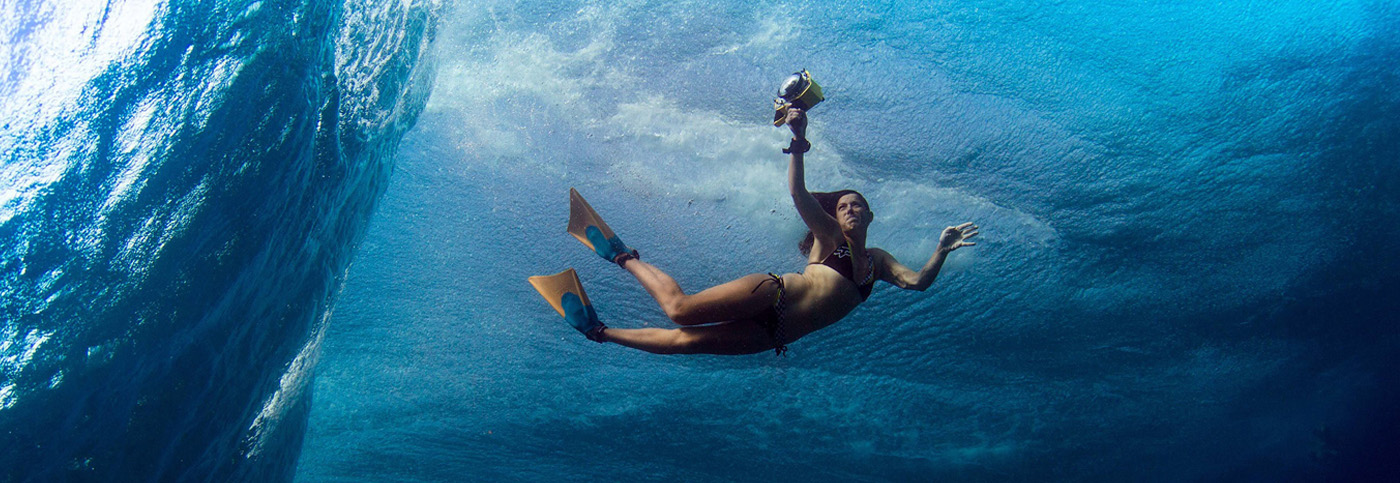 An underwater photograph showing a woman holding a camera with an underwater case, she is wearing a bikini and flippers. Lucia Griggi underwater photographer.