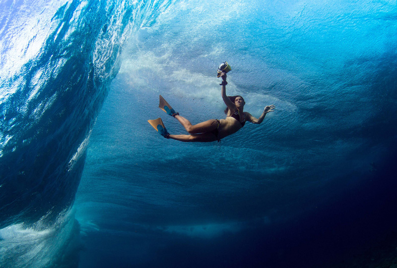 An underwater photograph showing a woman holding a camera with an underwater case, she is wearing a bikini and flippers. Lucia Griggi underwater photographer.