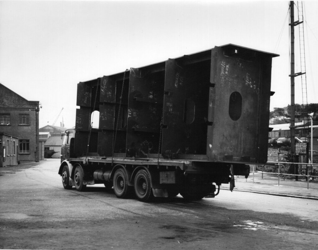 A black and white photograph showing a section of the Dock Gate arriving at Falmouth Docks on a lorry.