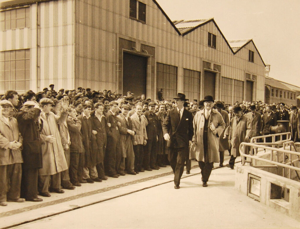 A Black and White photograph showing HRH Prince Philip, Duke of Edinburgh and Mr HAJ Silley, Chairman of Falmouth Docks and Engineering Company at the naming ceremony of the Queen Elizabeth Dock with a crowd of onlookers.