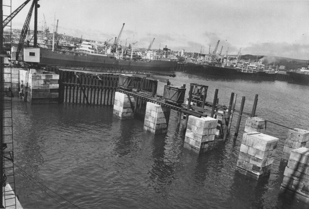 A black and white photograph showing a dam construction in the water.