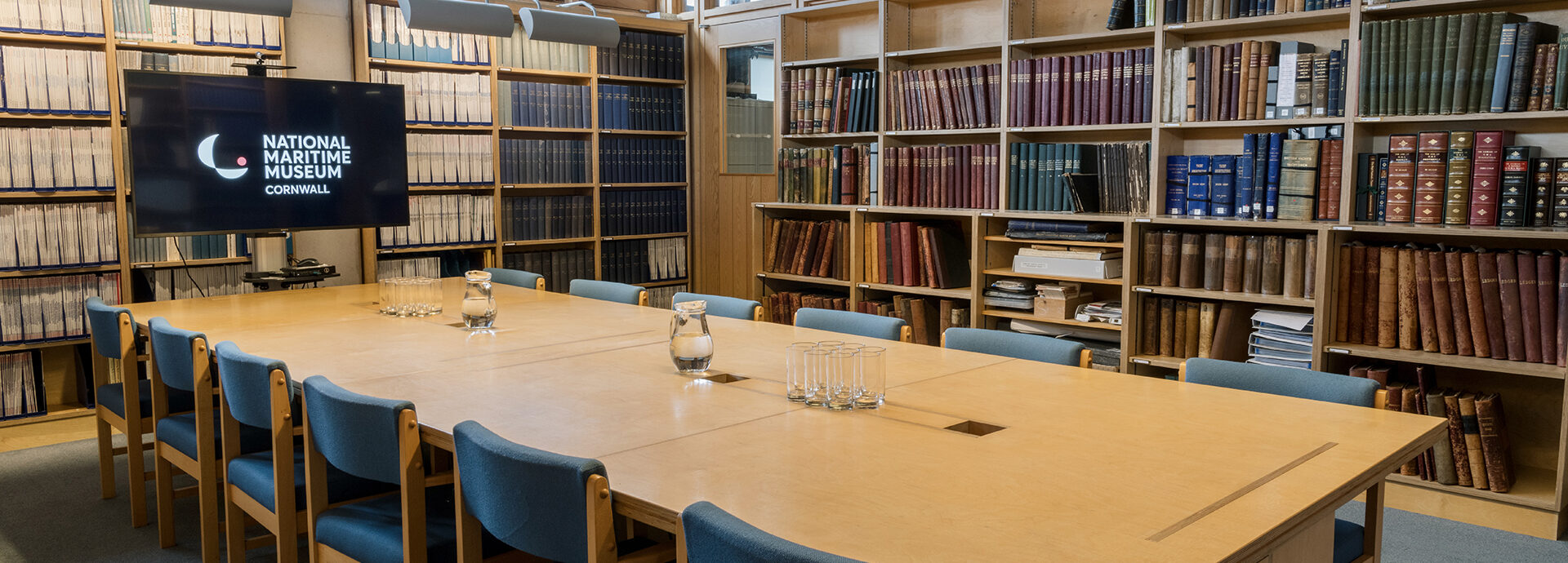 A large table with 12 chairs around it sits in the middle of a room lined with bookcases.