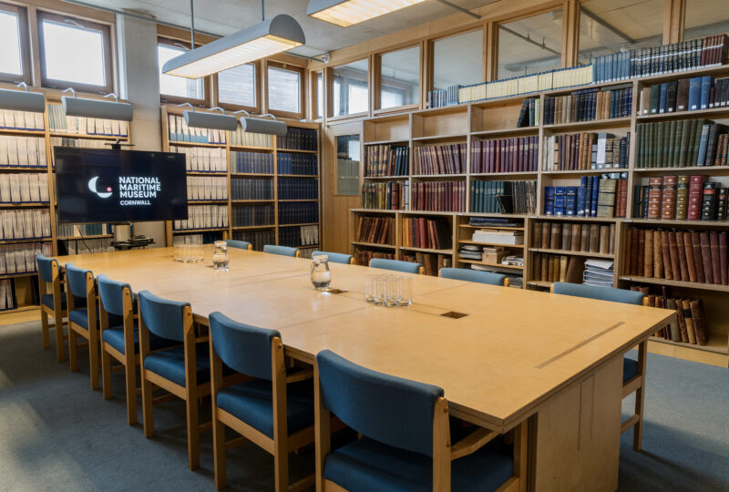 A large table with 12 chairs around it sits in the middle of a room lined with bookcases.