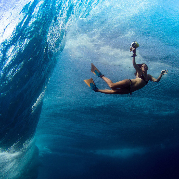 An underwater photograph showing a woman holding a camera with an underwater case, she is wearing a bikini and flippers. Lucia Griggi underwater photographer.