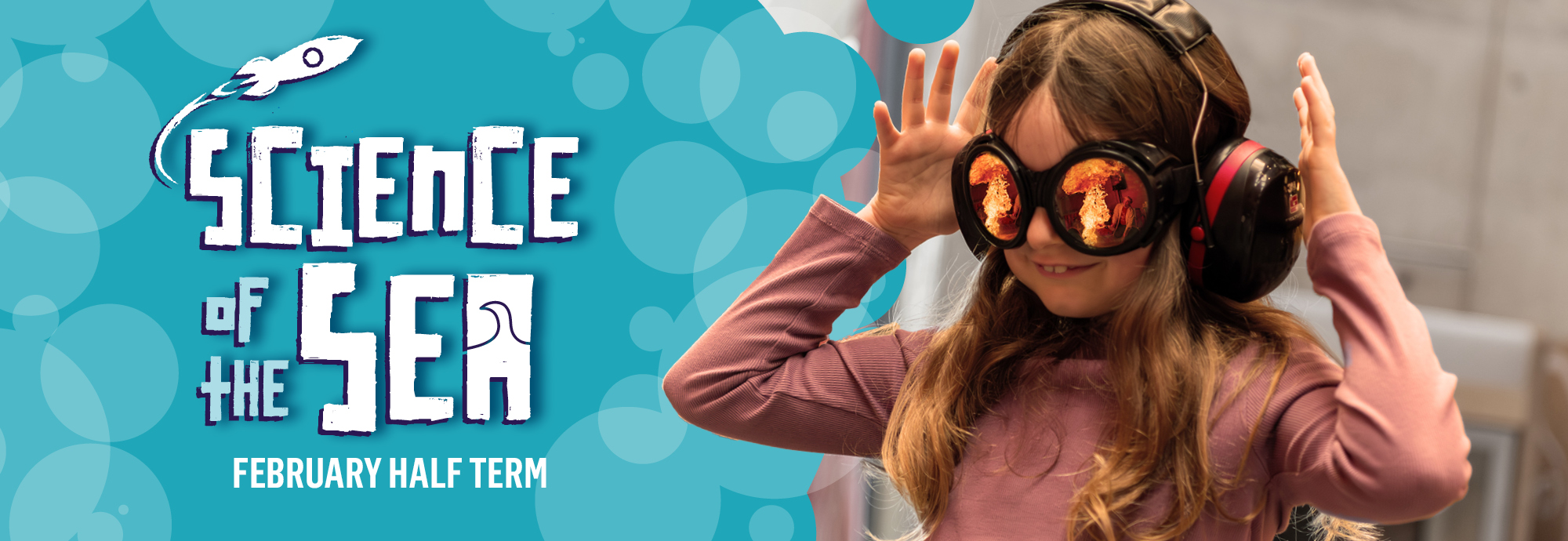 On the left hand side of a poster white text on a turquoise background of bubble shapes reads 'Science of the Sea - February Half Term' with a rocket illustration shooting of the words. On the right hand side a girl wearing ear defenders and eye goggles holds her hands up in the air smiling, and the reflection in her goggles shows a burst of flames from a science experiment.