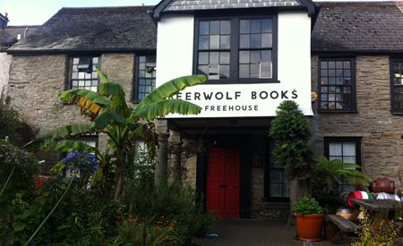 A photograph shows an old building freshly painted white with palms and other large plants in front of it.