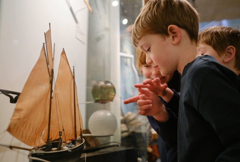 Young children are looking and pointing at a model shop in a glass cabinet.