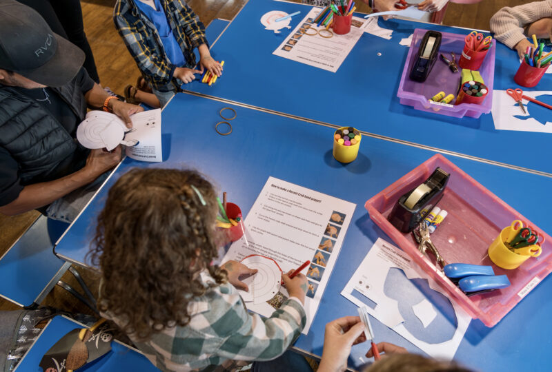 A photograph of families and children using art supplies while sitting around a table.