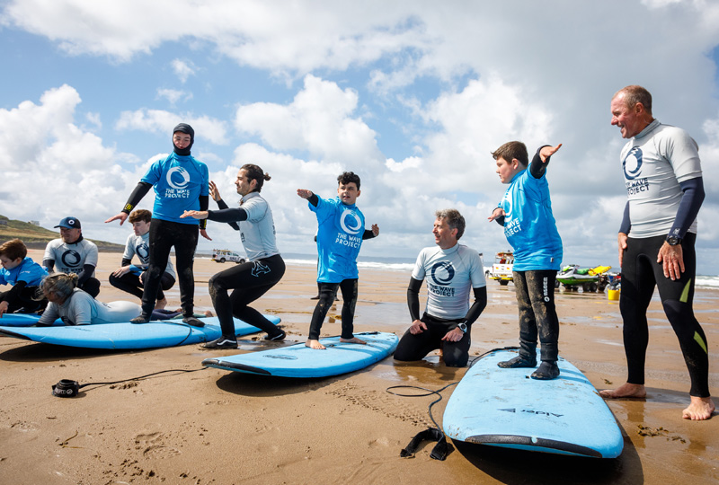 A photograph showing a group of people on a beach being taught how to stand on their surfboards, learning to surf.