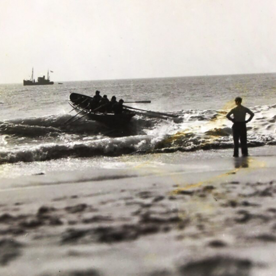 An old black and white photo of a person watching a rowing boat enter the water