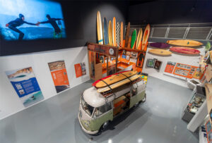 A photograph of the SURF! exhibition from above, showing a VW Campervan and surfboard display.