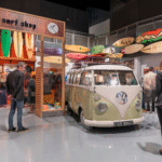 An exhibition of surfboards displayed on the wall surround a mint condition VW vintage campervan
