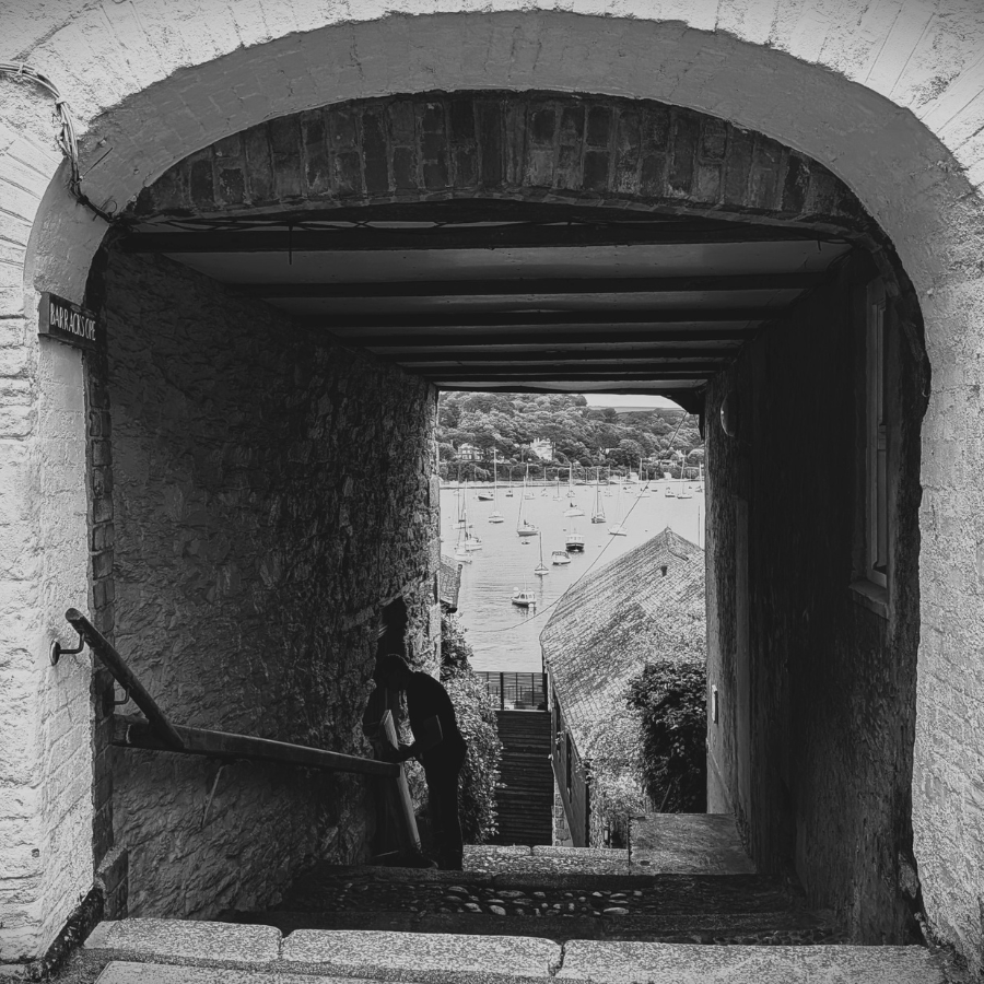 A black and white photograph shows the view through a dark opeway in Falmouth to the Fal river beyond.
