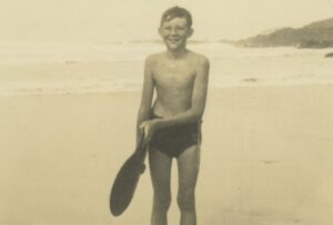 An archive photograph of a boy holding a bellyboard on a beach at Treyarnon, Cornwall, featured in Surfing Memories Exhibition at National Maritime Museum Cornwall