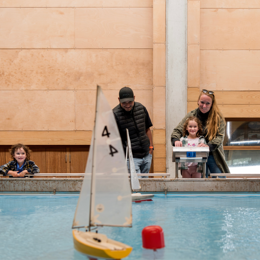 A family with two children enjoying sailing model boats on the Boat Pool at National Maritime Museum Cornwall.