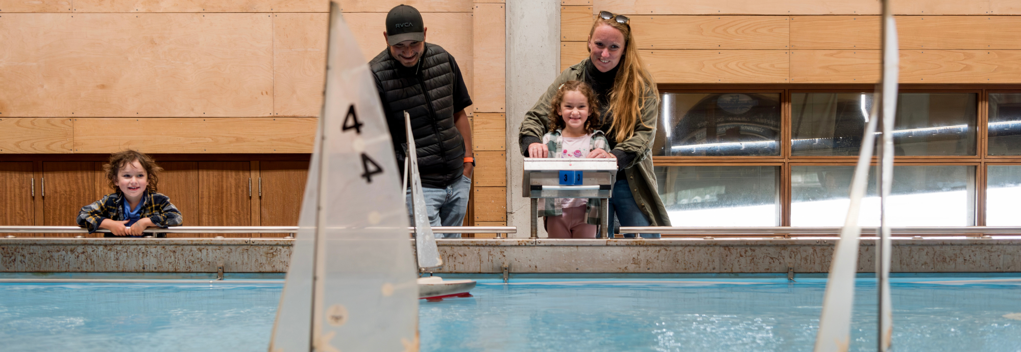 A family with two children enjoying sailing model boats on the Boat Pool at National Maritime Museum Cornwall.