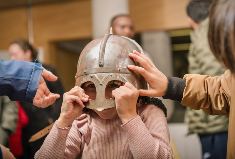 A young girl tries on a Viking Helmet during an object handling session at National Maritime Museum Cornwall.