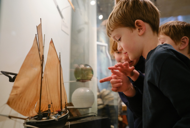 A group of children look and point at model boats in a display cabinet at National Maritime Museum Cornwall