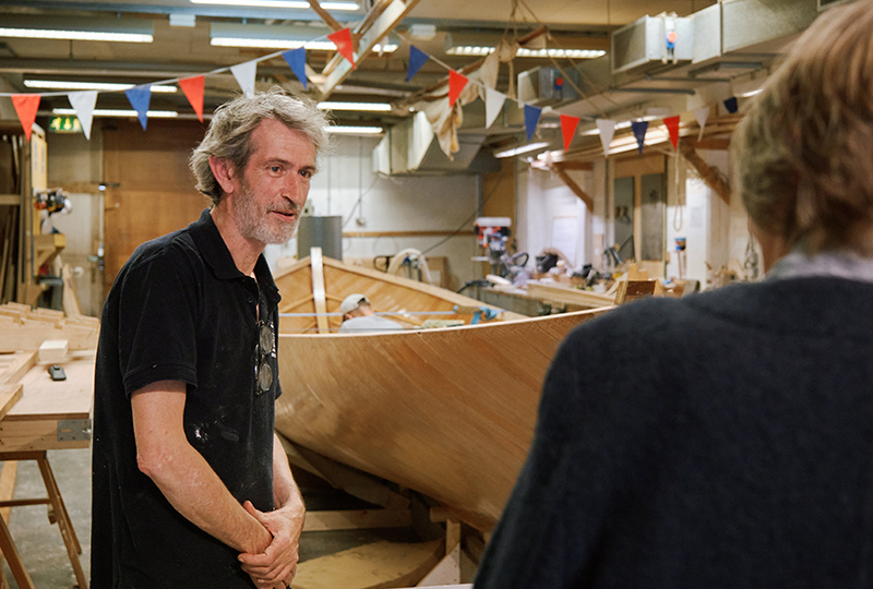 A man, who is a member of the museum team, and in a blue pop shirt, is talking to a member of the public.
