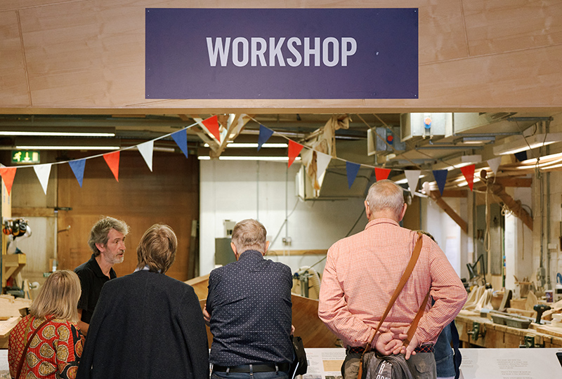 A group of people are talking with a member of the museum team. There is a big sign above them with 'workshop' written on it.