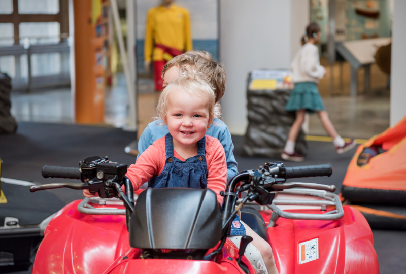 A small child smiles while sitting on an RNLI Quad Bike on display in the Rescue Zone at National Maritime Museum Cornwall.