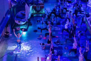 A group of people face a demonstrating yoga instructor, beside boat displays at NMMC at the Deep Blue Silent Disco Yoga event.