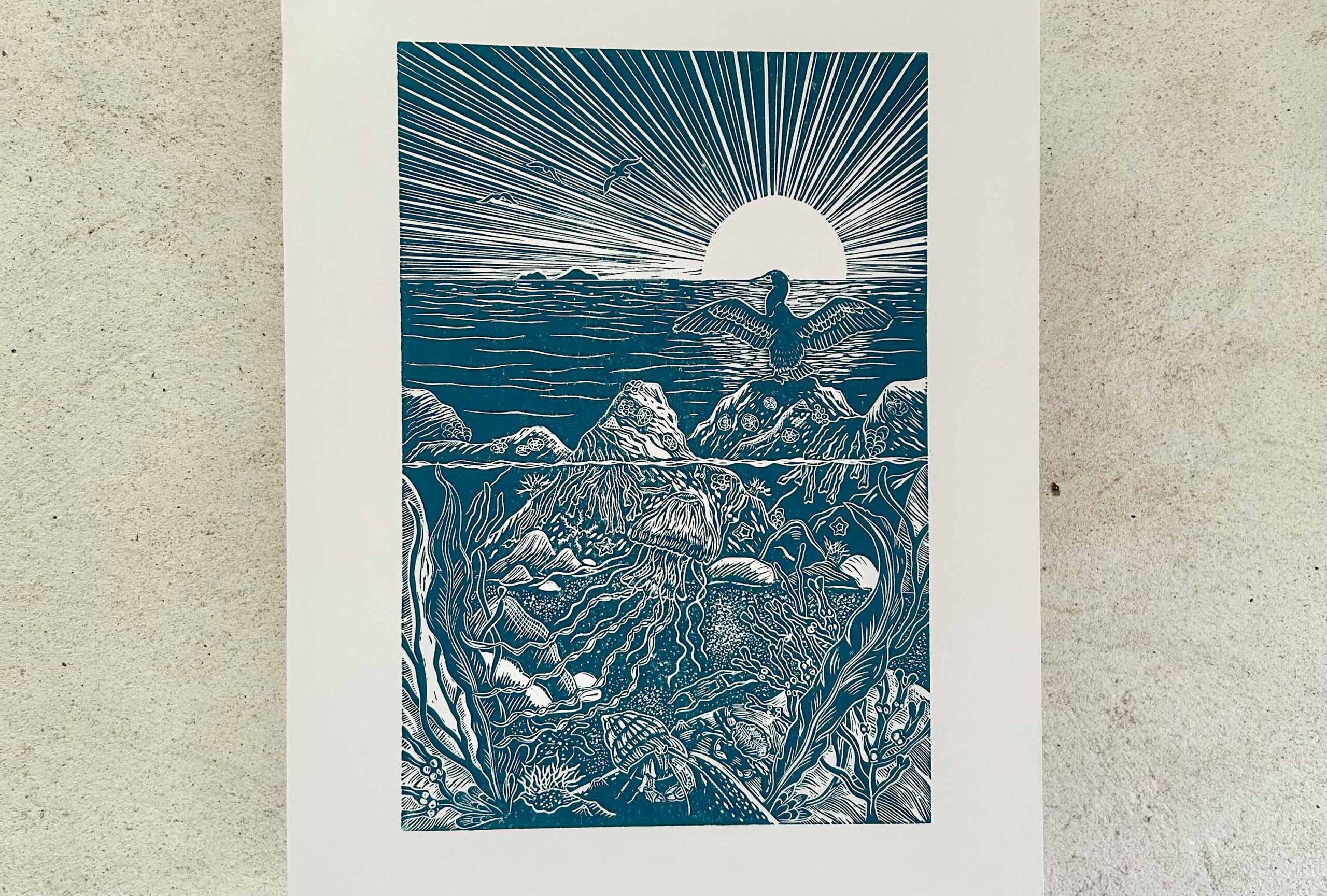 A photo of a linocut print with a landscape design in blue against a white background.