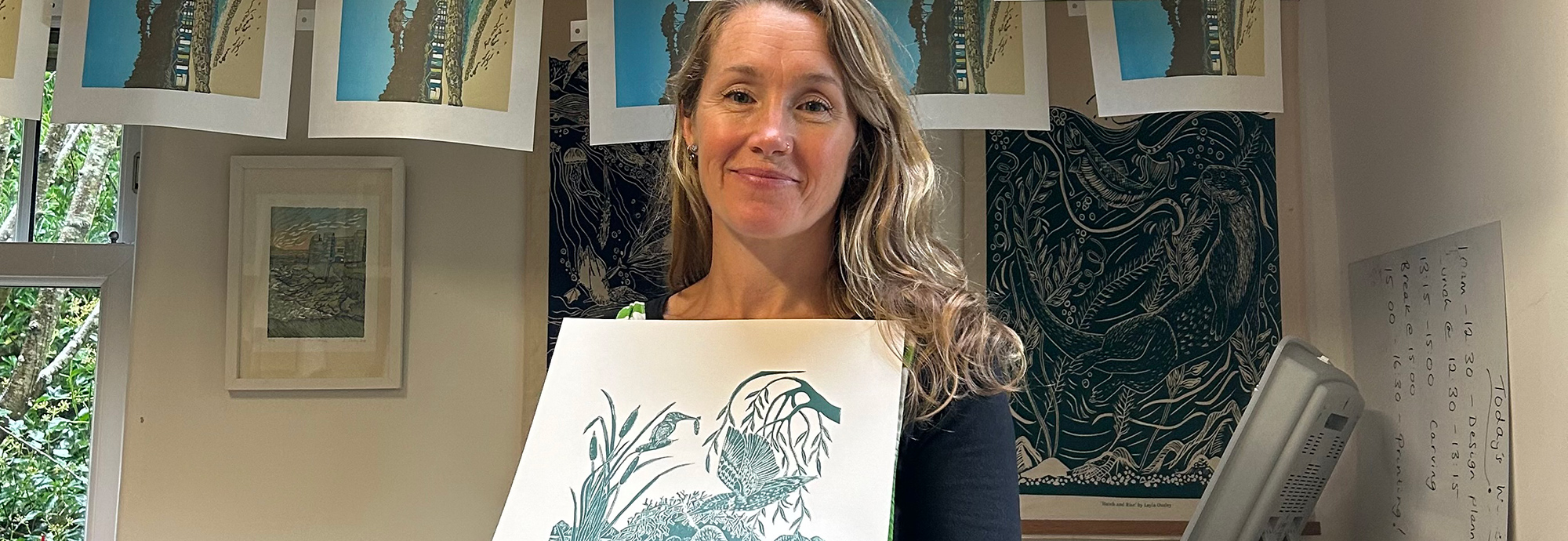A photo of a women holding a linocut print with more prints hanging from a drying line behind her.