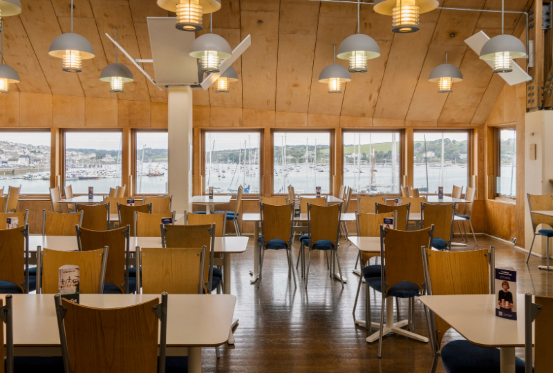 A view of cafe tables in Waterside Cafe at National Maritime Museum Cornwall, the windows show a view to Falmouth Harbour.