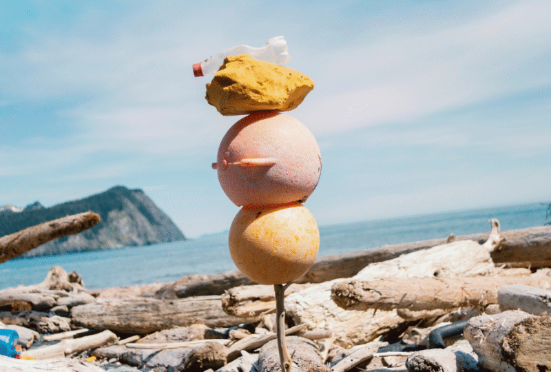 Gore Point Beach Alaska, 2013 A photographic artwork by Andy Hughes show plastic flotsam and jetsam stacked vertically on a stake of driftwood with a dramatic ocean landscape in the background.