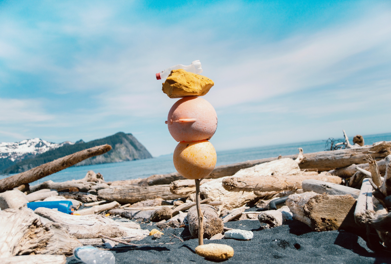 Gore Point Beach Alaska, 2013 A photographic artwork by Andy Hughes show plastic flotsam and jetsam stacked vertically on a stake of driftwood with a dramatic ocean landscape in the background.